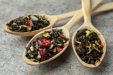 Photo of Different kinds of dry herbal tea in wooden spoons on light grey table, closeup