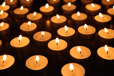 Photo of Burning tealight candles on dark surface, closeup