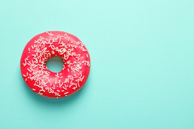 Delicious glazed doughnut with sprinkles on color background, top view