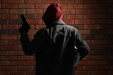 Thief in hoodie with gun against red brick wall, back view