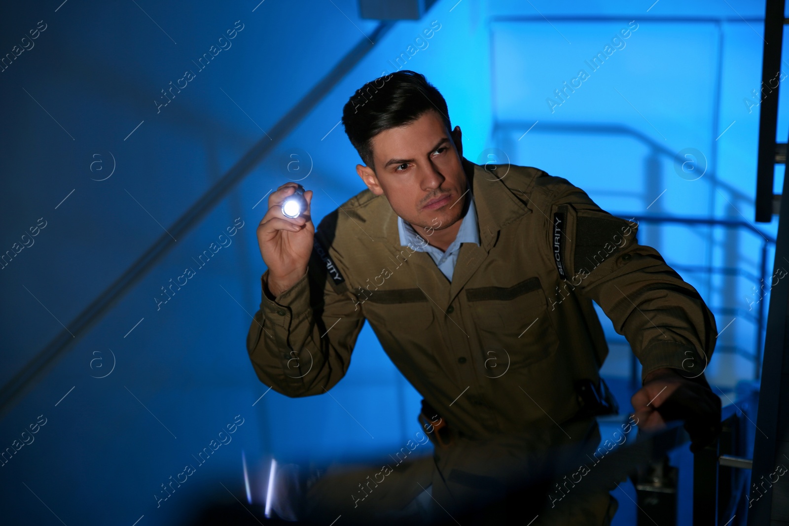 Photo of Professional security guard with flashlight on stairs in dark room