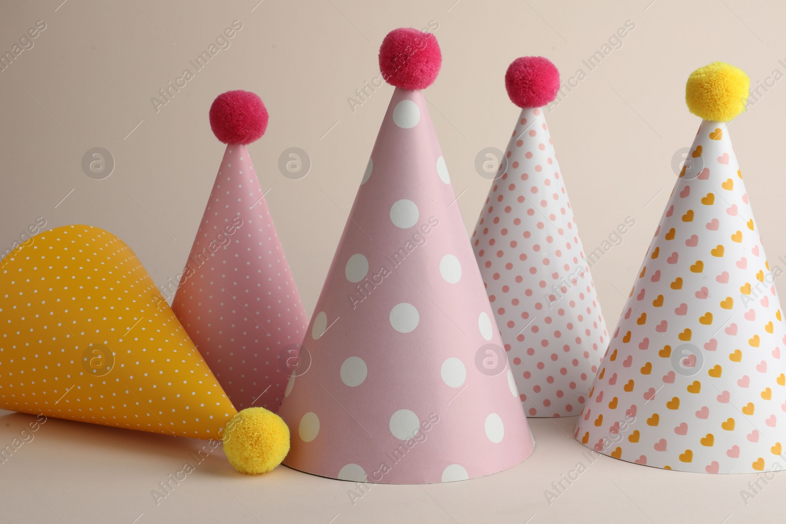 Photo of Beautiful party hats with pompoms on beige background