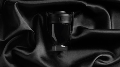 Photo of Luxury bottle of perfume on black silk, top view