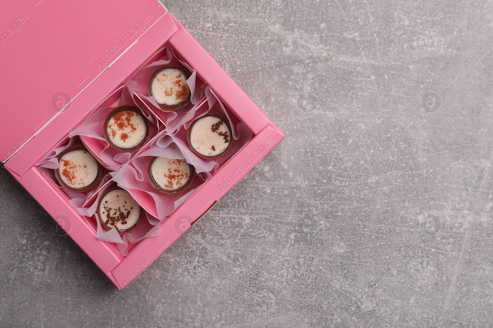 Photo of Delicious chocolate candies in pink box on light grey table, top view and space for text