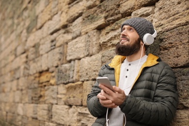 Photo of Mature man with headphones listening to music near stone wall. Space for text