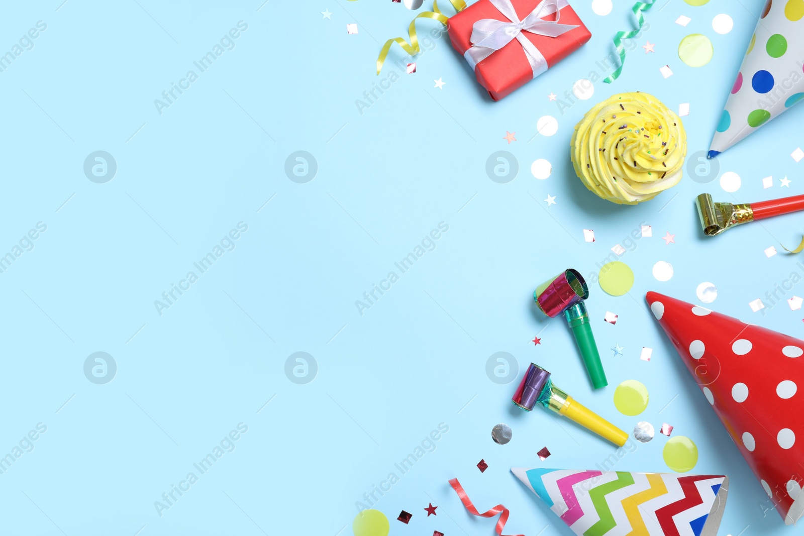 Photo of Flat lay composition with party hats, birthday decor and cupcake on light blue background. Space for text