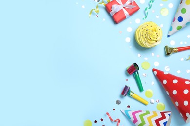 Photo of Flat lay composition with party hats, birthday decor and cupcake on light blue background. Space for text