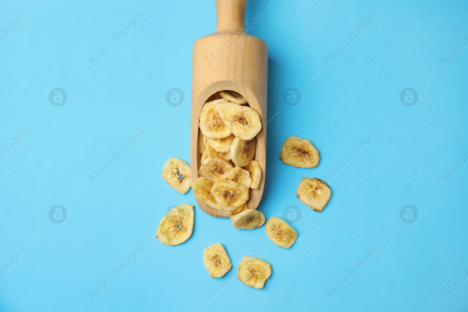 Photo of Wooden scoop with banana slices on color background, top view. Dried fruit as healthy snack