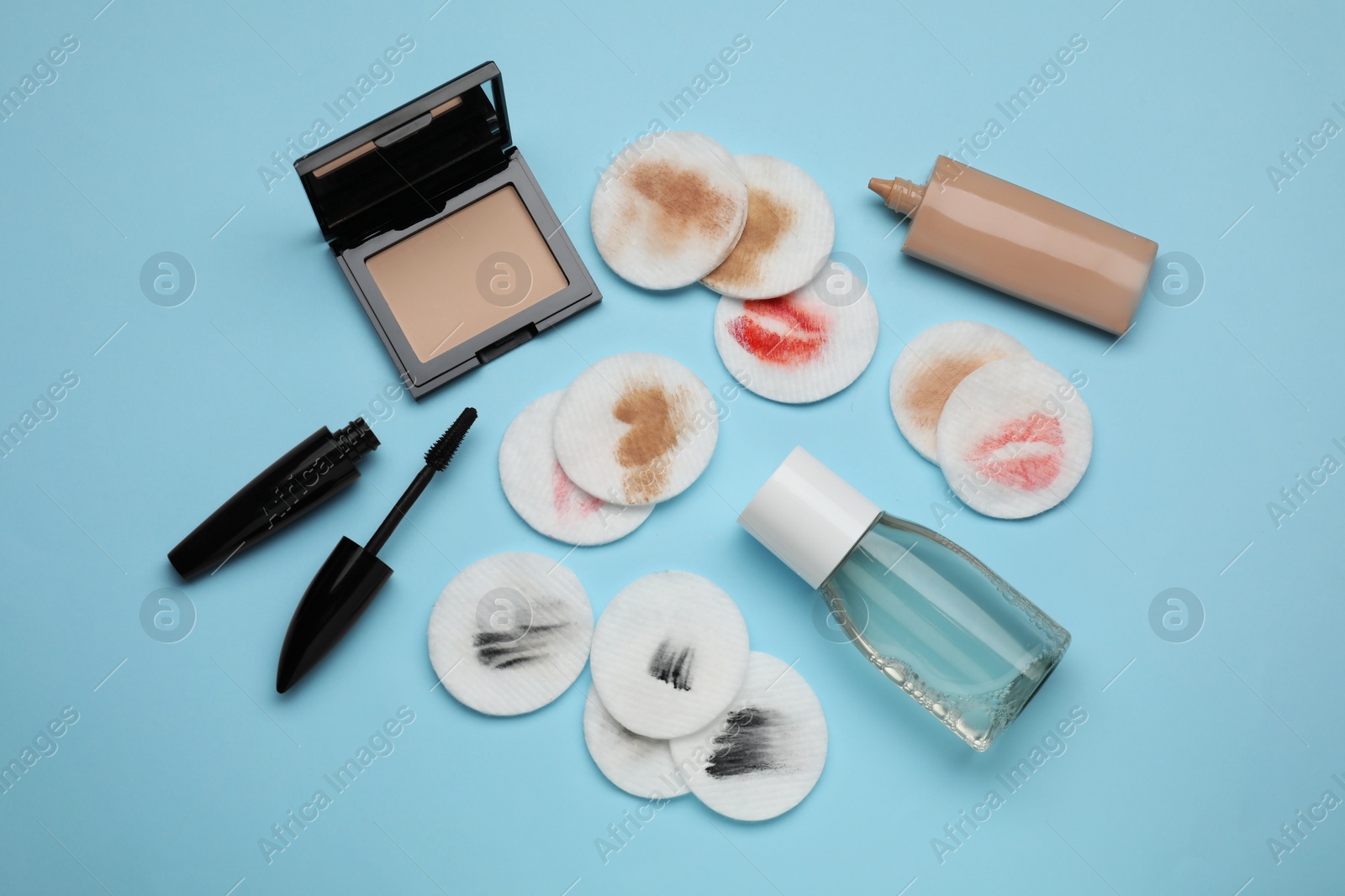 Photo of Bottle of makeup remover, dirty cotton pads and different products on light blue background, flat lay