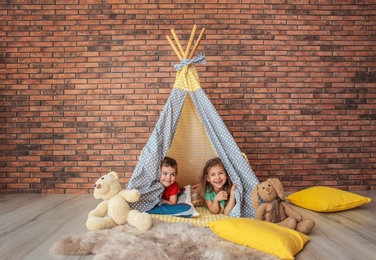 Photo of Playful little children in handmade tent indoors