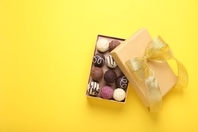 Photo of Open box with delicious chocolate candies on yellow background, top view. Space for text