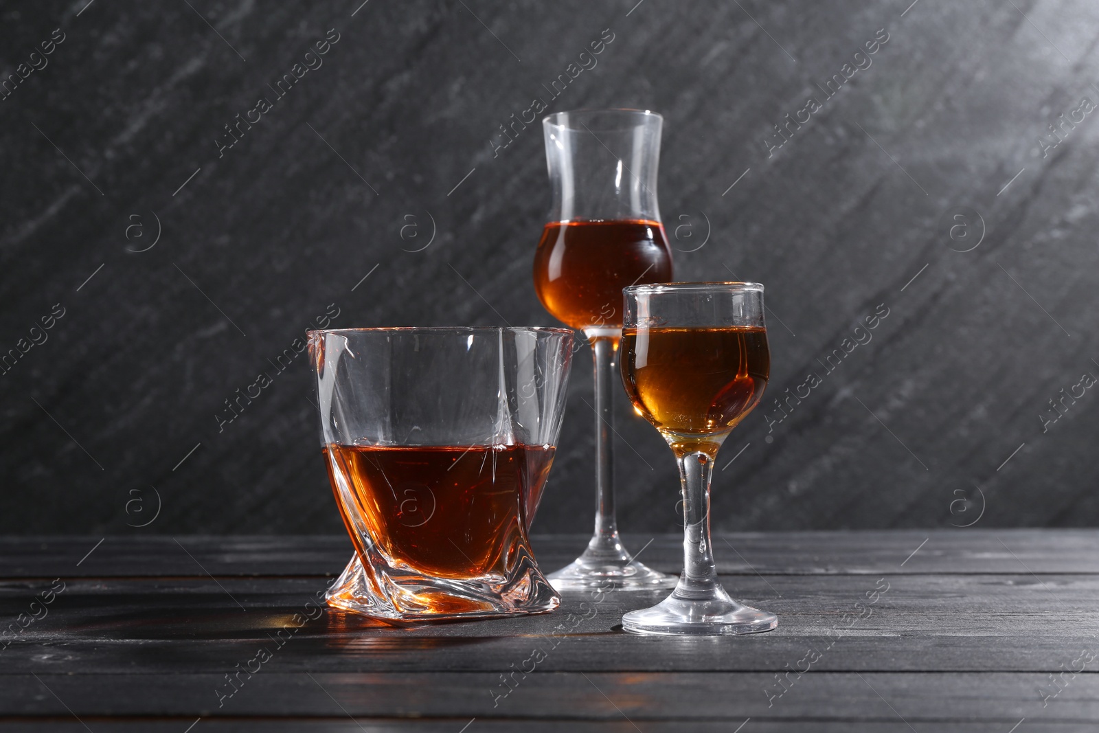 Photo of Different delicious liqueurs in glasses on black wooden table