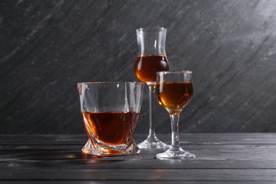 Photo of Different delicious liqueurs in glasses on black wooden table