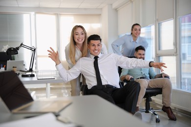 Happy office employees riding chairs at workplace