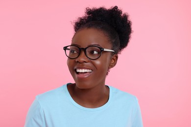 Portrait of happy young woman in eyeglasses on pink background