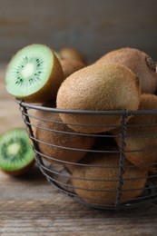 Photo of Metal basket with cut and whole fresh kiwis on wooden table, closeup