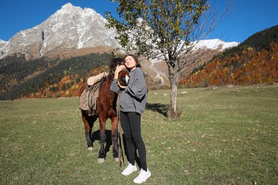 Young woman hugging horse in mountains on sunny day. Beautiful pet