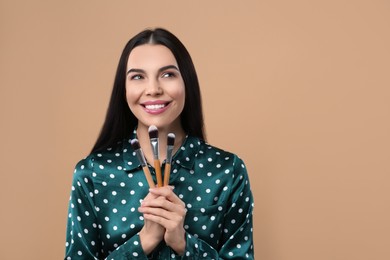 Happy woman with different makeup brushes on light brown background, space for text