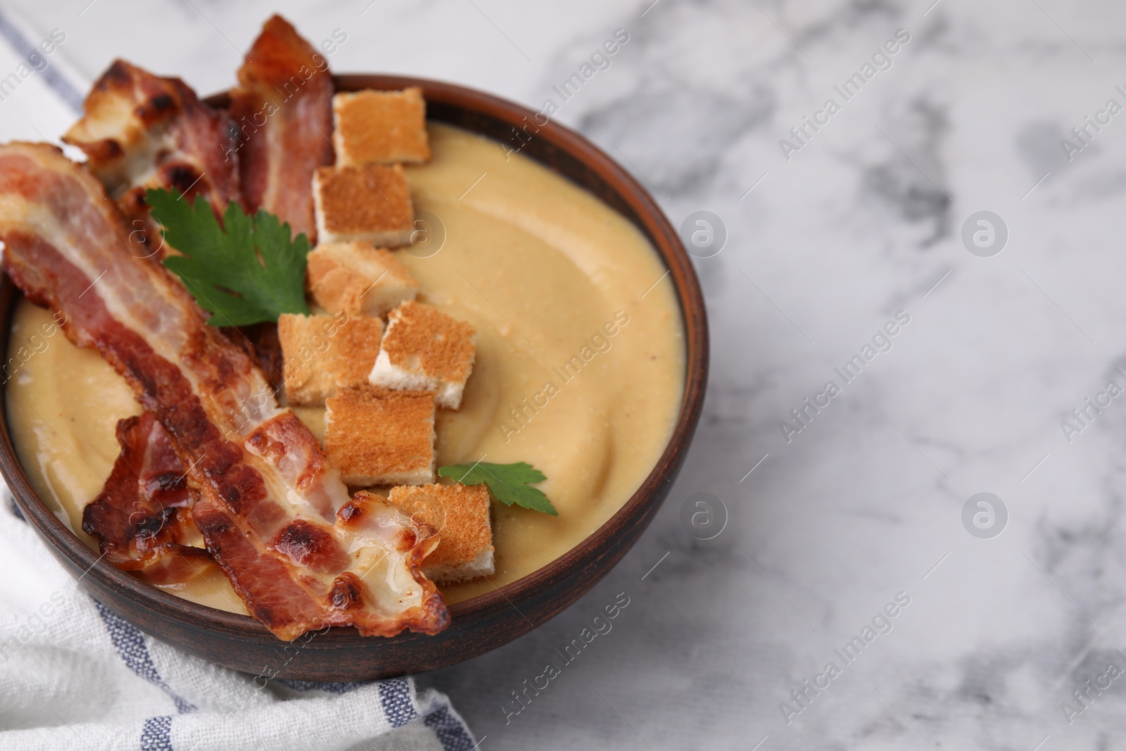 Photo of Delicious lentil soup with bacon and parsley in bowl on light marble table, closeup. Space for text