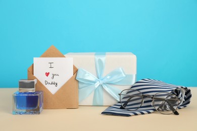 Photo of Happy Father's Day. Card with phrase I Love You, Daddy in envelope, tie, glasses, perfume and gift box on beige table
