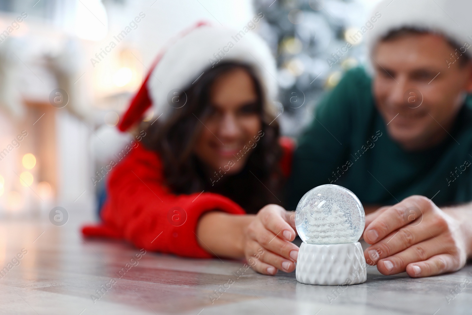 Photo of Happy couple on floor indoors, focus on hands with snow globe