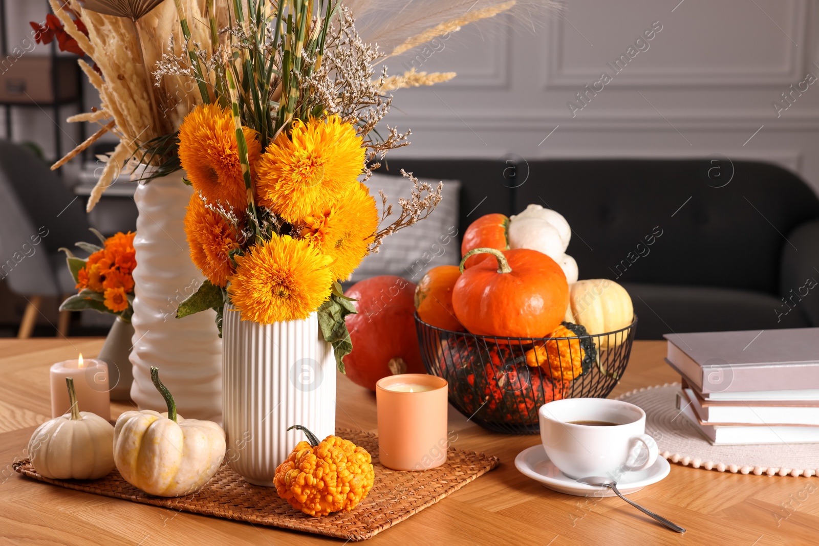 Photo of Beautiful autumn composition with bright orange flowers, pumpkins and burning candles on wooden table in room