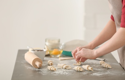 Woman preparing tasty croissants on table in kitchen, closeup