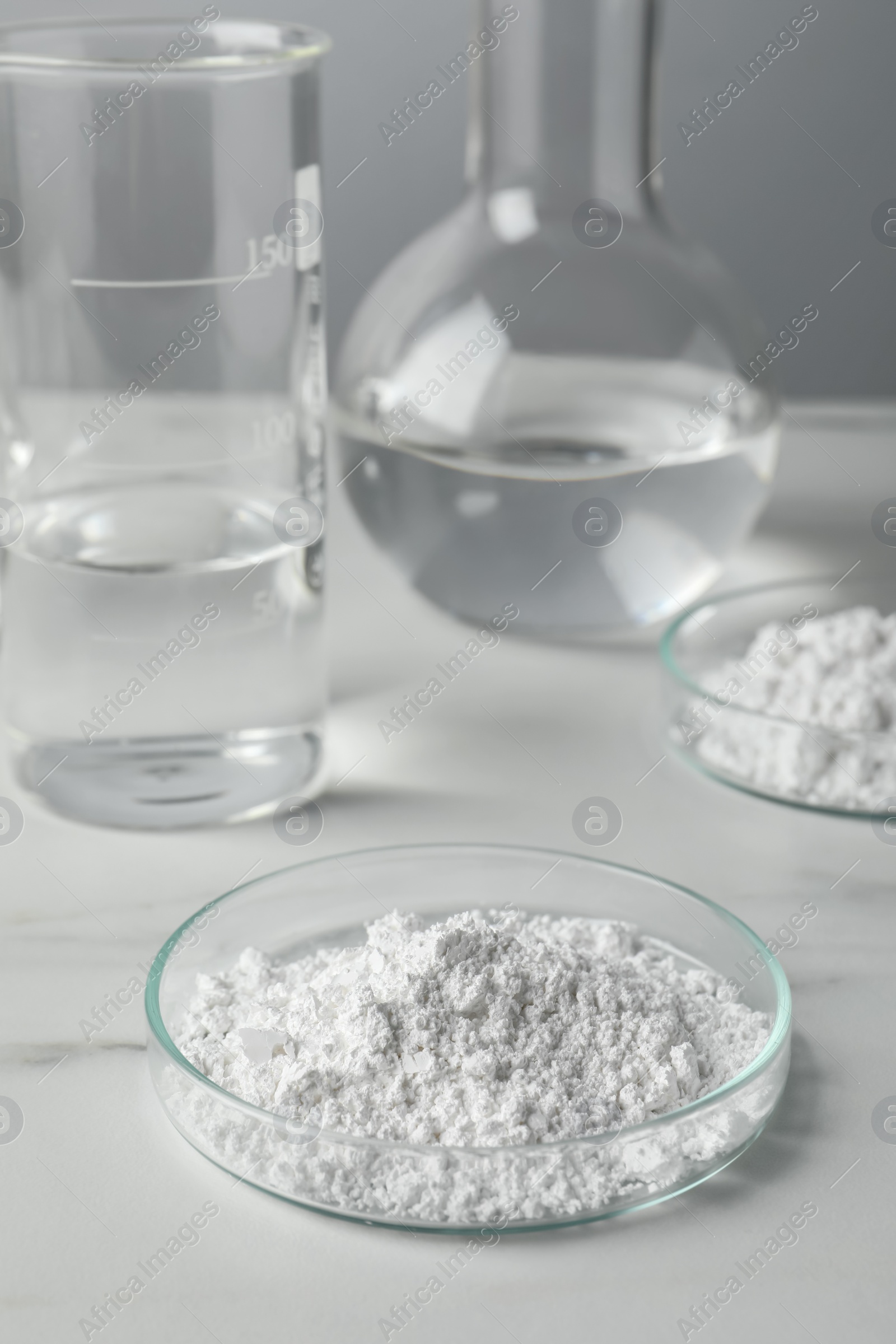 Photo of Petri dishes with calcium carbonate powder and laboratory glassware on white marble table