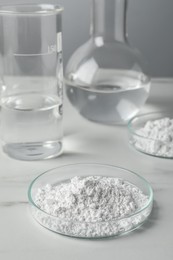 Petri dishes with calcium carbonate powder and laboratory glassware on white marble table