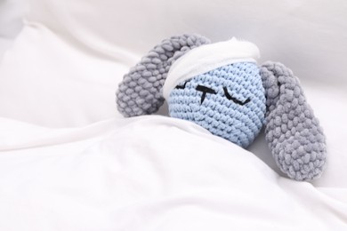 Photo of Toy cute bunny with bandage under blanket in bed