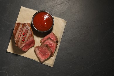 Photo of Delicious grilled beef steak with spices and tomato sauce on dark gray table, top view. Space for text