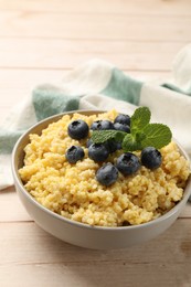 Photo of Tasty millet porridge with blueberries and mint in bowl on light wooden table, closeup