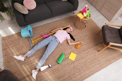 Photo of Tired young woman sleeping and cleaning supplies on floor in living room, above view