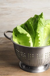 Photo of Colander with fresh leaves of green romaine lettuce on wooden table