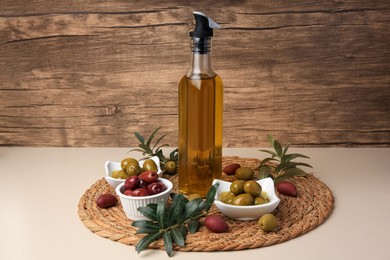 Photo of Bottle of oil, olives and tree twigs on beige table