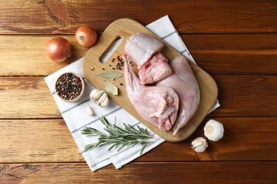 Photo of Fresh raw rabbit meat and spices on wooden table, flat lay