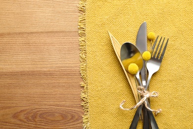 Set of cutlery, yellow cloth and autumnal decor on wooden background, flat lay with space for text. Table setting elements