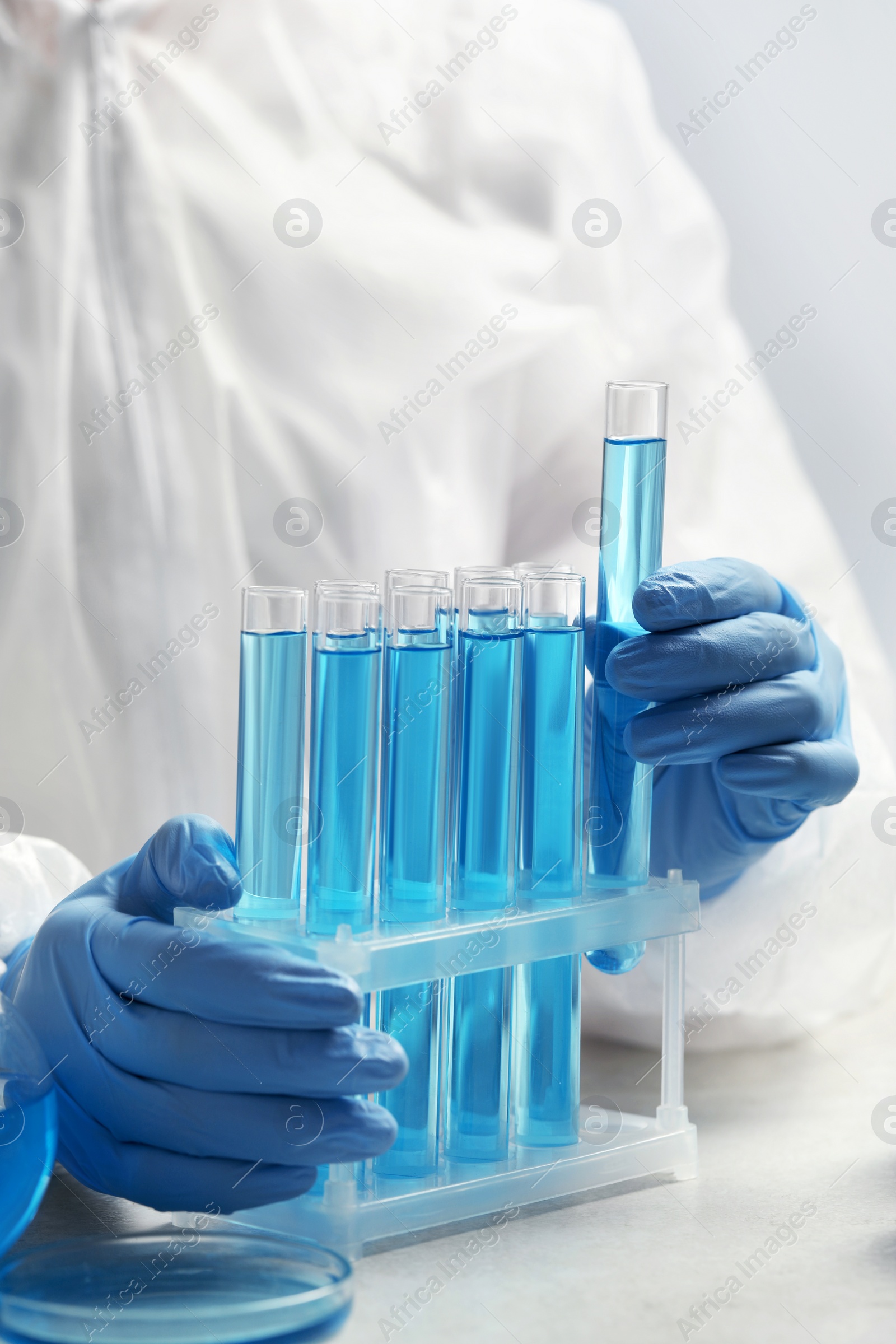 Photo of Scientist taking test tube with light blue liquid at white table in laboratory, closeup