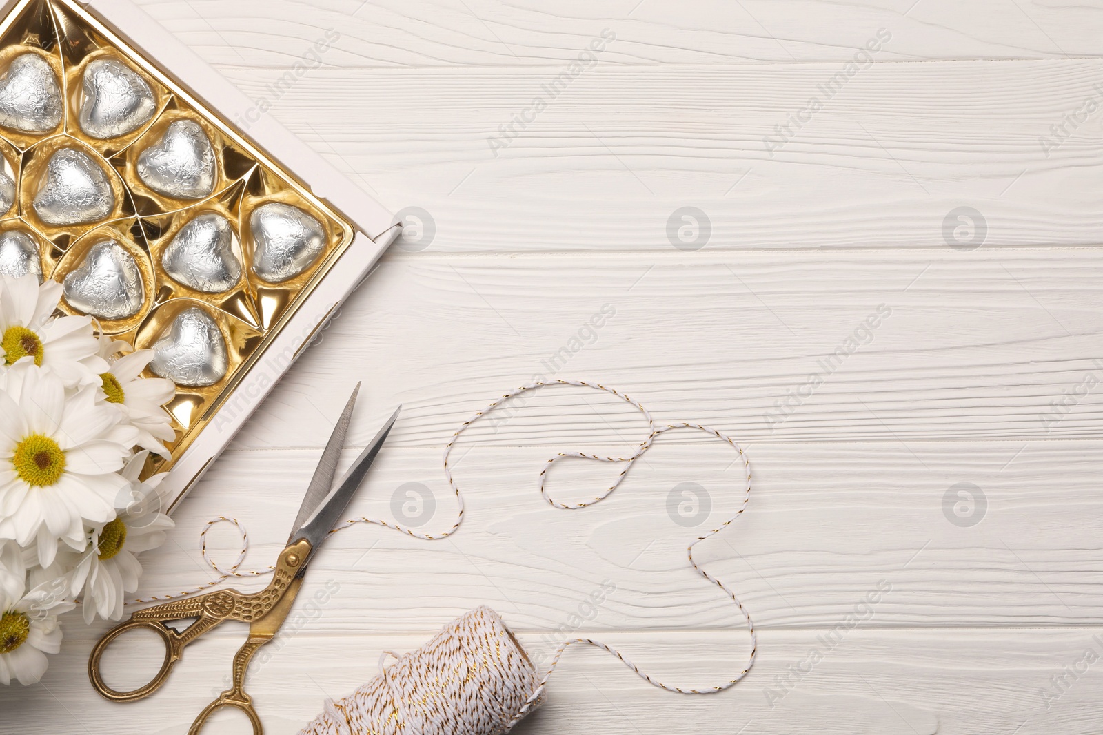 Photo of Delicious heart shaped chocolate candies, scissors and twine on white wooden table, flat lay. Space for text