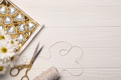 Delicious heart shaped chocolate candies, scissors and twine on white wooden table, flat lay. Space for text