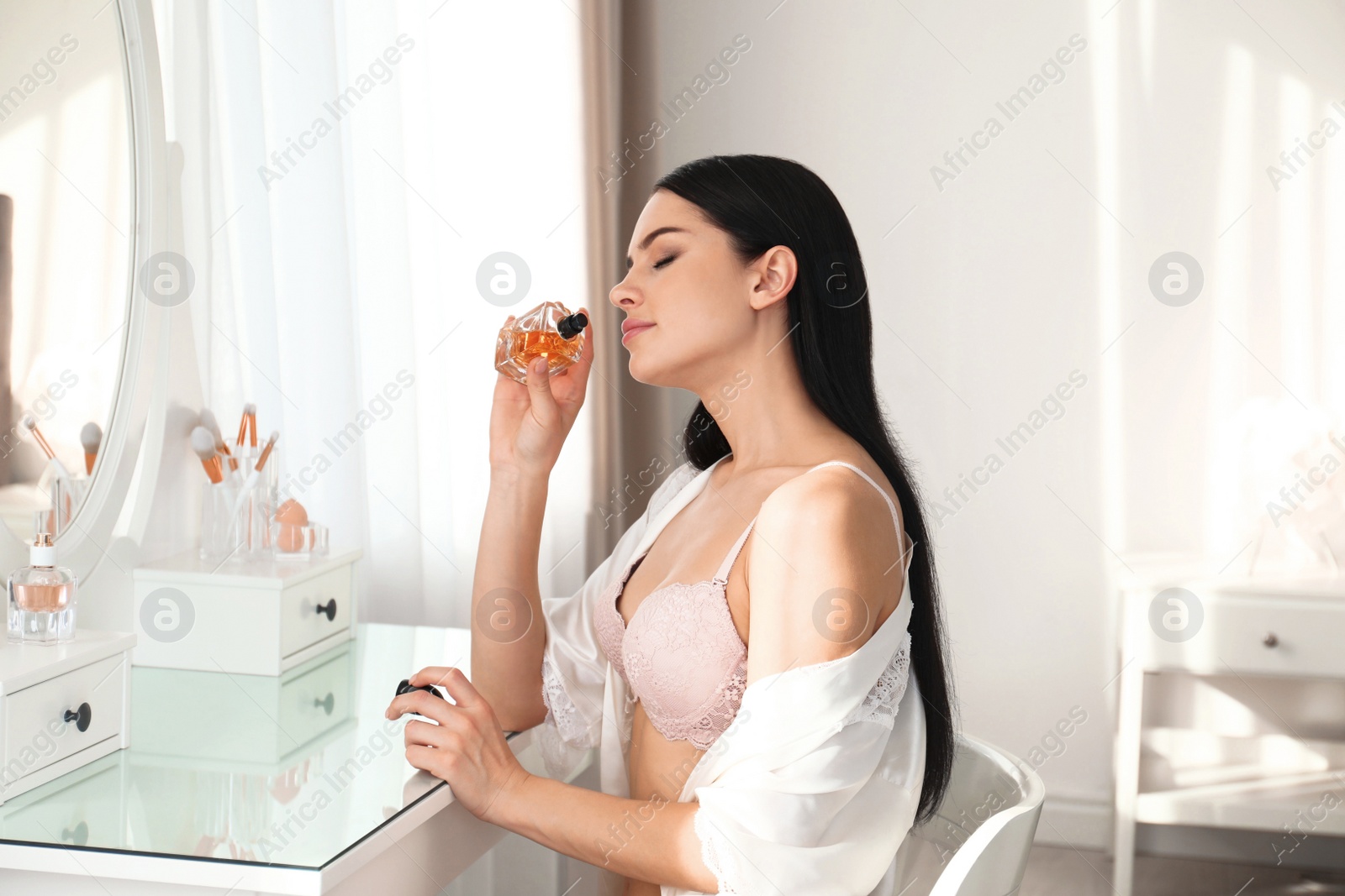 Photo of Beautiful young woman in pink underwear applying perfume at home