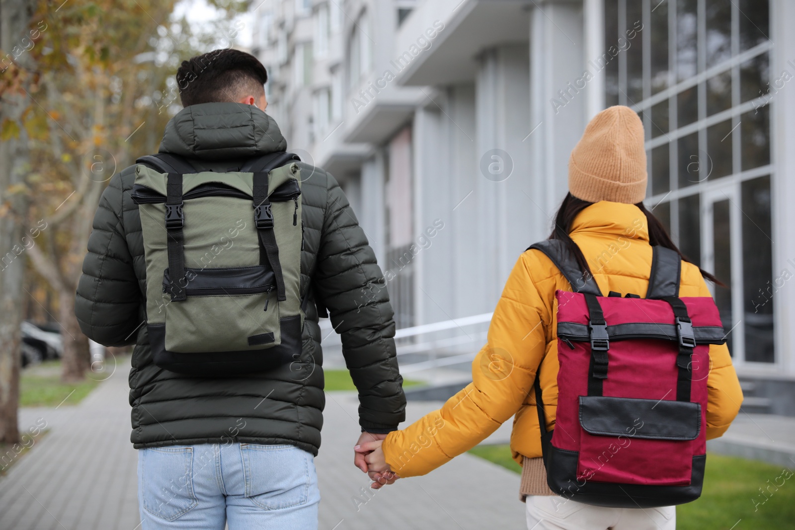 Photo of Couple with travel backpacks on city street, back view. Urban trip