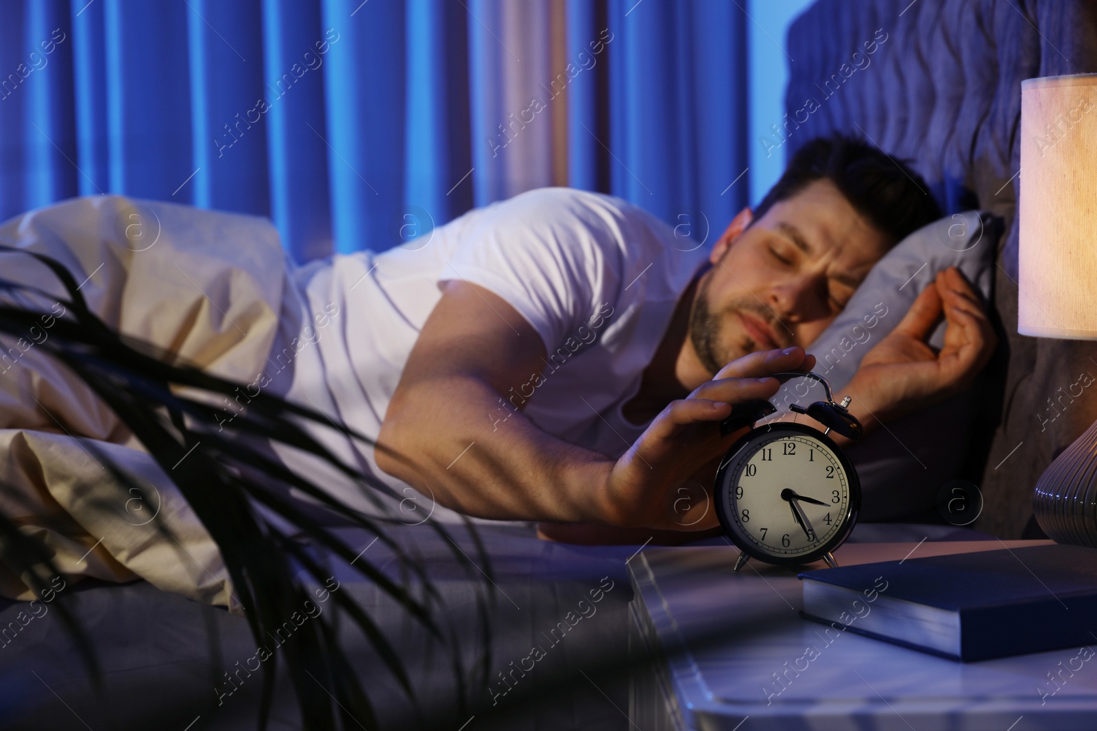 Photo of Sleepy man turning off alarm clock in dark room. Bedtime