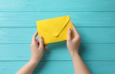 Photo of Woman with yellow paper envelope at light blue wooden table, top view