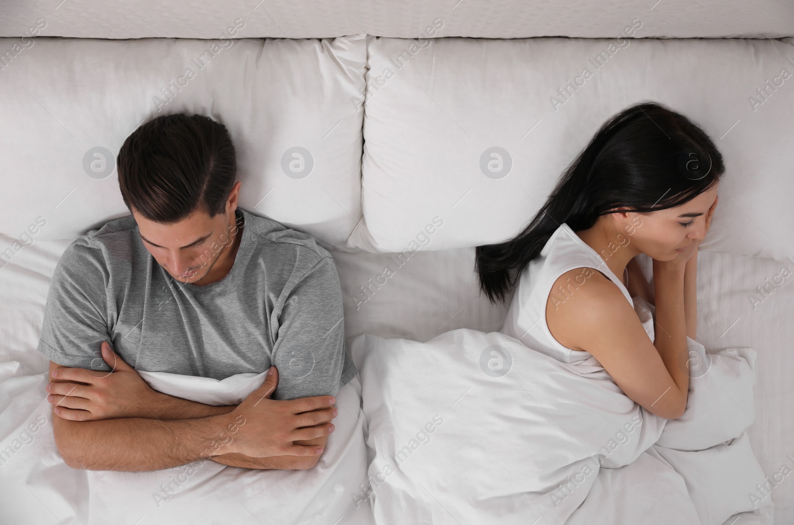 Photo of Unhappy couple with relationship problems after quarrel in bed, above view