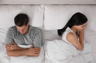Photo of Unhappy couple with relationship problems after quarrel in bed, above view