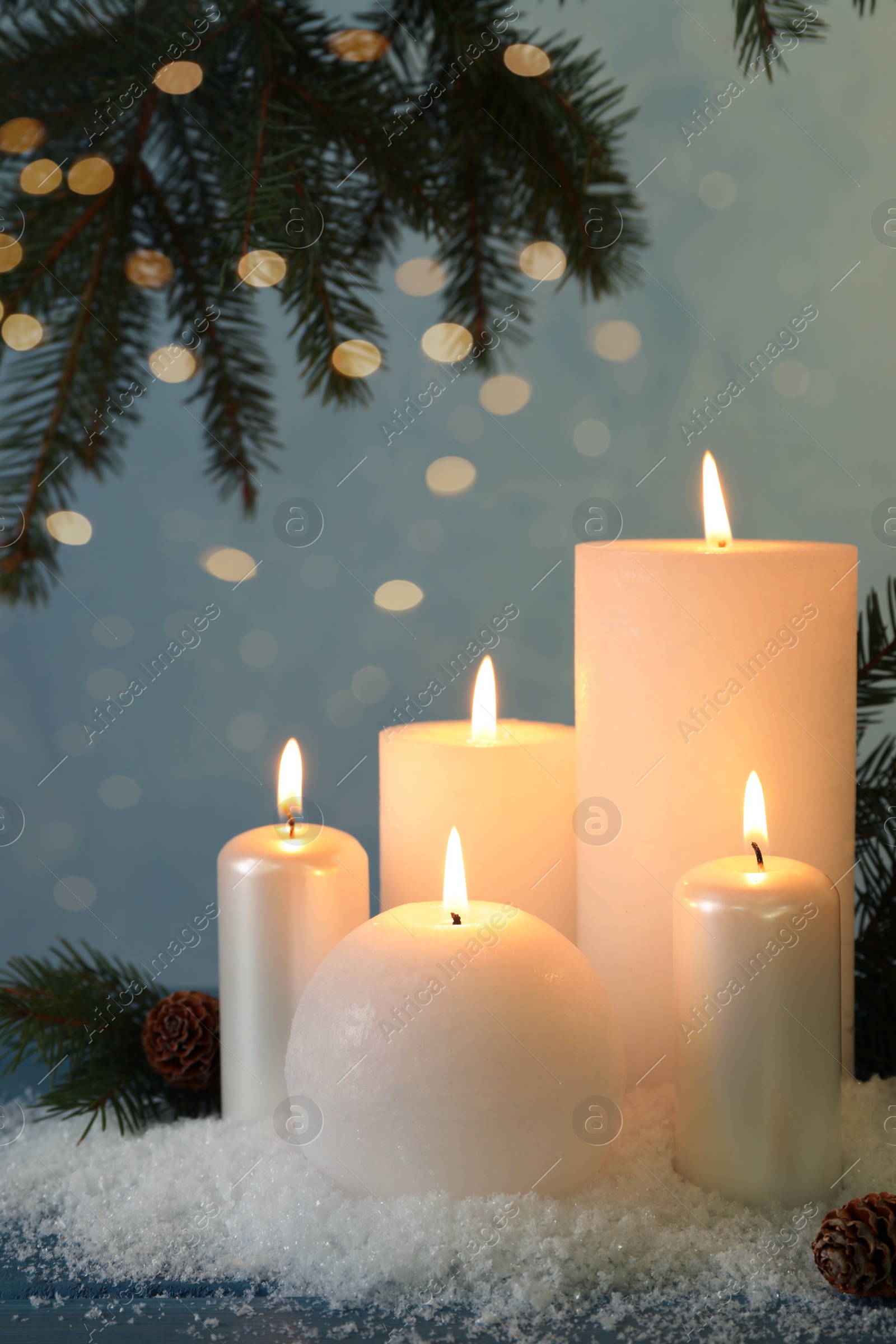 Photo of Burning candles with fir tree branch, cones and artificial snow on blue wooden table. Christmas atmosphere