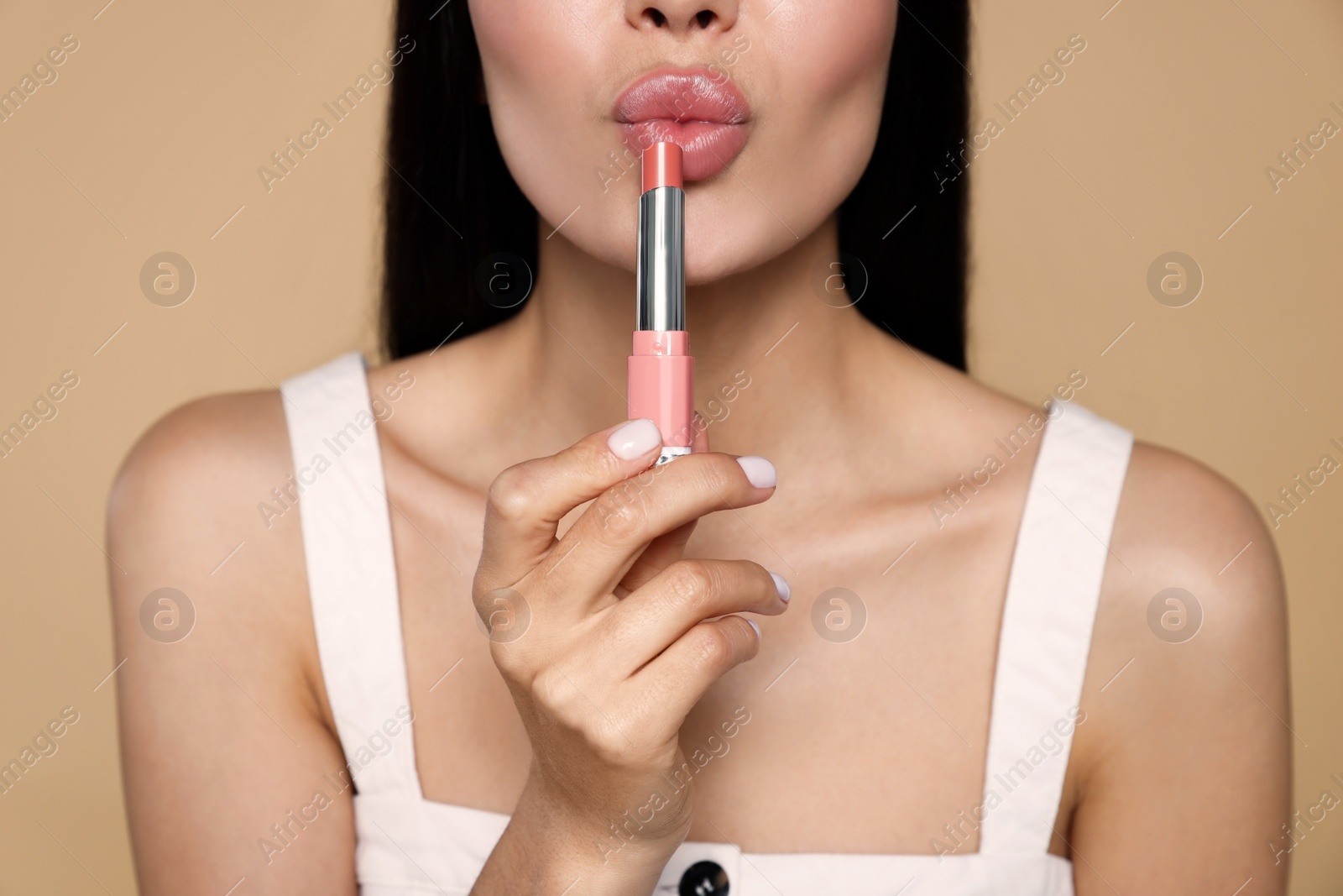 Photo of Young woman with beautiful makeup holding nude lipstick on beige background, closeup