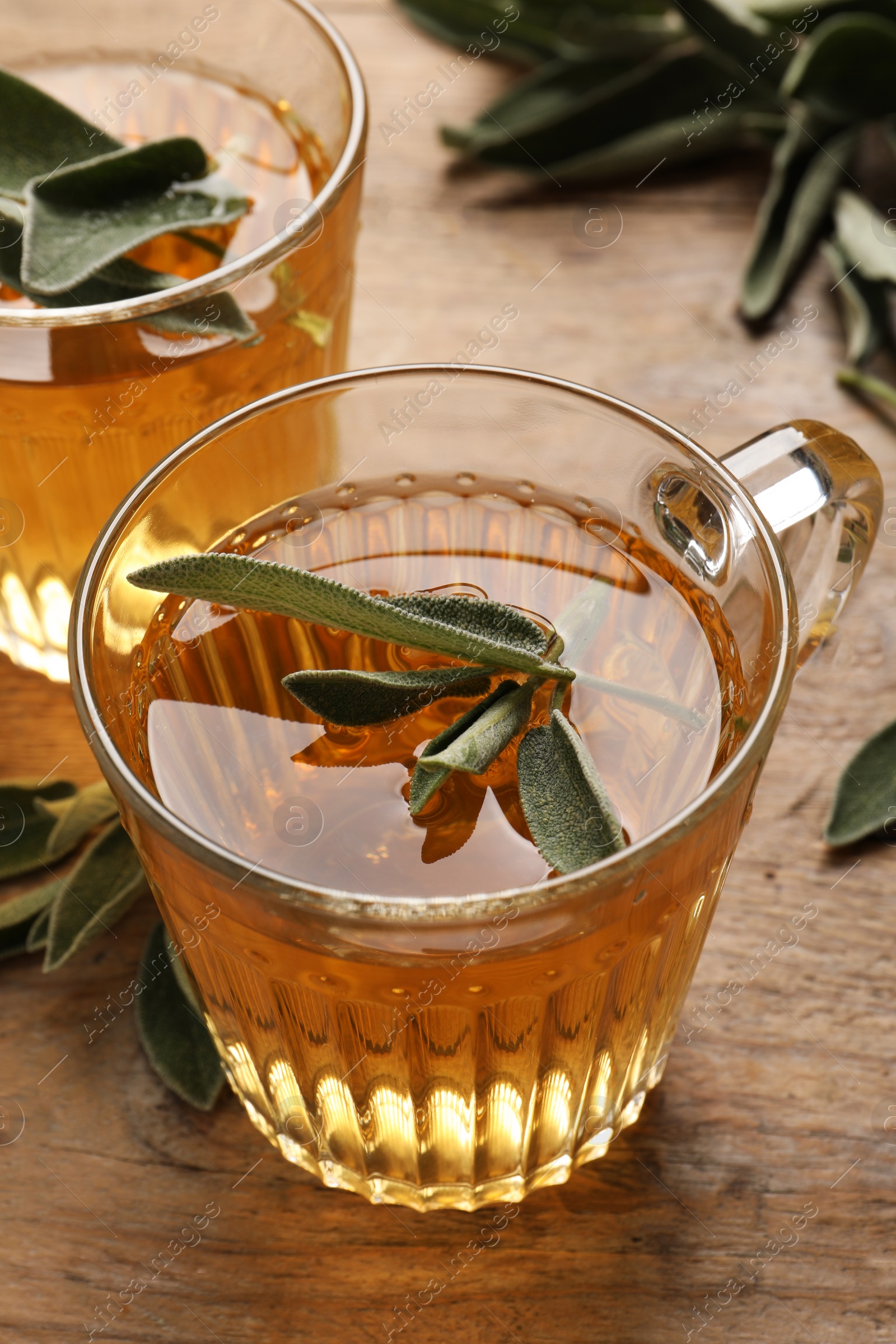 Photo of Cups of aromatic sage tea with fresh leaves on wooden table, closeup