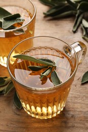 Photo of Cups of aromatic sage tea with fresh leaves on wooden table, closeup